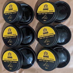 May include: Six circular black containers of Vaidya Vitality Pure Shilajit Resin, each with a yellow lid featuring the brand logo, text, and a mountain graphic. Each lid is labeled 20g, and the open containers reveal a dark, viscous substance.