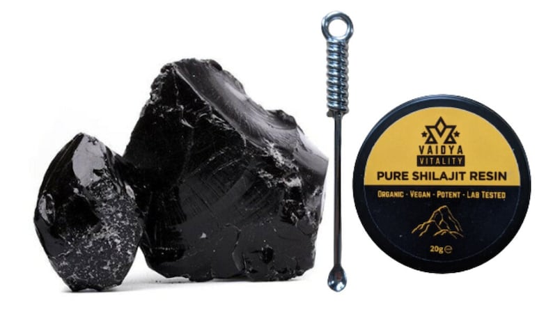May include: Two large, glossy, black resinous chunks next to a silver metal applicator tool and a round black container with a yellow label reading Vaidya Vitality Pure Shilajit Resin, Organic, Vegan, Potent, Lab Tested, and 20g.