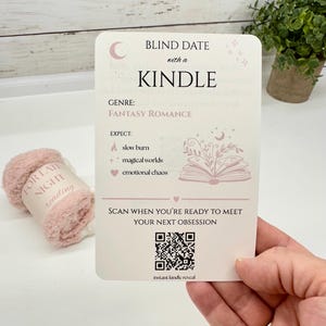 May include: A rectangular white card titled Blind Date with a Kindle, featuring the genre Fantasy Romance, a list of expectations including slow burn, magical worlds, and emotional chaos, a QR code, and the text Scan when you're ready to meet your next obsession.