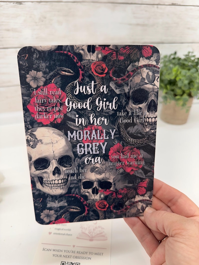 May include: A rectangular card featuring a dark, gothic-inspired print with skulls, red roses, butterflies, and snakes. The text reads: "I still read fairy tales, they're just darker now", "Just a Good Girl in her MORALLY GREY era", "take it like a Good Girl", "you had me at trigger warning", and "touch her and die".