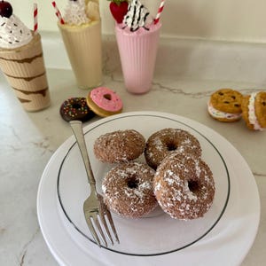 May include: An assortment of miniature desserts, including chocolate-covered donuts dusted with powdered sugar on a white plate with a fork. Milkshakes with whipped cream, cherries, and strawberries are also visible.
