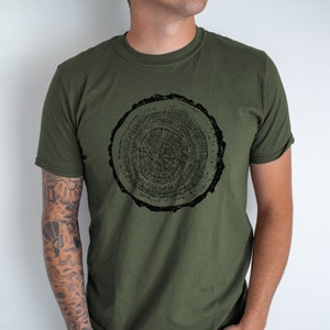 May include: A green t-shirt with a black print of a tree trunk cross-section. The print shows the rings of the tree.