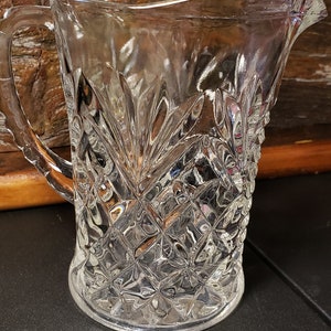 May include: A clear glass pitcher with a diamond pattern. The pitcher has a handle and a wide mouth.
