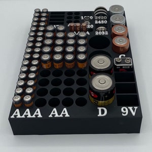 May include: Black battery organizer with compartments for AAA, AA, D, and 9V batteries. The organizer has labels for each type of battery and includes numbers indicating the quantity of each battery type.