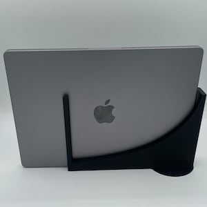 May include: A black laptop stand with a curved design, holding a silver laptop with an Apple logo. The stand is made of a sturdy material and provides a comfortable viewing angle for the laptop.