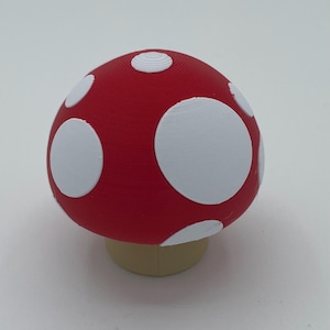 May include: A red and white mushroom-shaped object with white polka dots. The mushroom has a tan base.