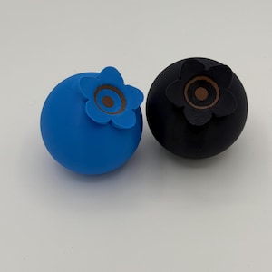 May include: Two blueberry-shaped ornaments, one blue and one black, with a brown flower design on top.