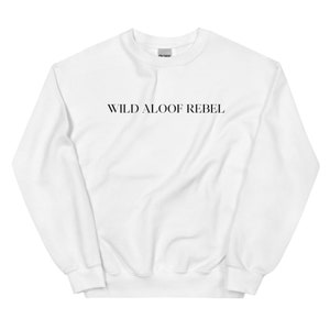 以下が含まれることがあります： 前面に黒い文字で「WILD ALOOF REBEL」とプリントされた白いクルーネックのトレーナーです。