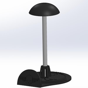 Puede incluir: Un soporte de casco negro con un logotipo de calavera y alas. El soporte tiene una parte superior redonda y una base con un diseño circular.