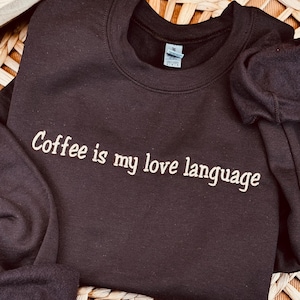 May include: A dark brown sweatshirt with the text "Coffee is my love language" in white embroidery.