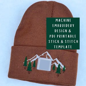 以下が含まれることがあります： 茶色のニット帽。山と木の刺繍デザインが施されています。折り返しのつばがあり、緑色の長方形に「MACHINE EMBROIDERY DESIGN & PDF PRINTABLE STICK & STITCH TEMPLATE」の文字が書かれています。