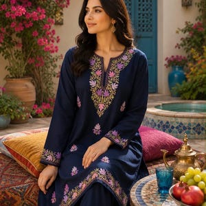 May include: A navy blue long-sleeved tunic and matching trousers set featuring a split neckline and intricate floral embroidery in shades of purple, pink, and green along the collar, cuffs, and hemline of the garment.