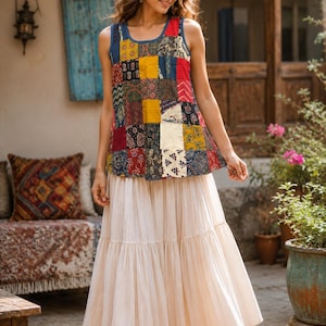 May include: A sleeveless tank top featuring a multi-colored patchwork design with various floral and geometric patterns in shades of red, blue, yellow, and black, paired with a long, solid cream-colored tiered skirt with a gathered, flowing hemline.