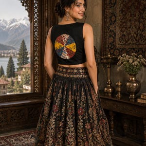 May include: A black sleeveless crop top featuring a circular multi-colored patchwork design on the back, paired with a matching black floor-length skirt adorned with an intricate floral pattern in red, gold, and green tones with a wide waistband.