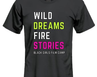 May include: A dark gray t-shirt with the text "WILD DREAMS FIRE STORIES" in white, green, and pink lettering. The text "BLACK GIRLS FILM CAMP" is printed in white below the other text.