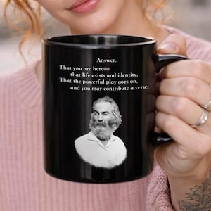 May include: Black ceramic mug featuring a portrait and quote. The mug has the text "Answer. That you are here—that life exists and identity. That the powerful play goes on, and you may contribute a verse."