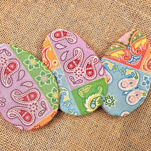 May include: Three colorful fabric Easter eggs with paisley patterns in shades of pink, blue, green, orange, and red.