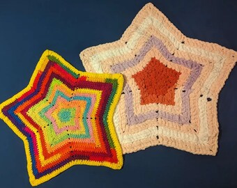 May include: Two crocheted star-shaped rugs. One rug is yellow with rainbow stripes and the other is pink with white and purple stripes.