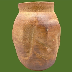 May include: A handmade, brown ceramic vase with a wide, rounded body and a narrow neck. The vase has a textured surface with visible horizontal lines and subtle colour variations. The overall shape is reminiscent of a traditional jar.