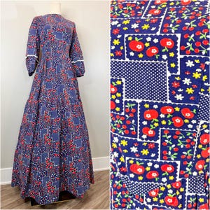 May include: A long, vintage blue dress with a patchwork pattern of red flowers, white polka dots, and square designs. The dress has long sleeves with white trim and a full skirt. The dress is displayed on a mannequin.