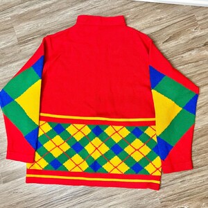May include: A red sweater with a high collar and colorful argyle pattern. The sleeves feature green, yellow, and blue diamond shapes. The lower section has a horizontal argyle design in the same colors.