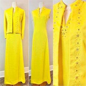 May include: A bright yellow floor-length sleeveless dress paired with a matching long-sleeved jacket. Both pieces feature a vertical band of floral embroidery accented with small clear rhinestones along the neckline and front edges.