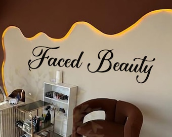 May include: Interior of a beauty salon with brown chairs, a manicure table, and a foot spa. The wall features the text "Faced Beauty" in elegant script. The space has a modern, minimalist design with neutral tones and bright lighting.