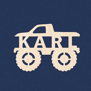 Op de afbeelding: Witte houten uitsnijding van een monstertruck met de naam "KART" erop.