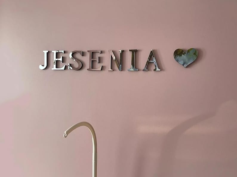 May include: A pink wall with the name "JESENIA" in silver letters and a silver heart with a floral design.
