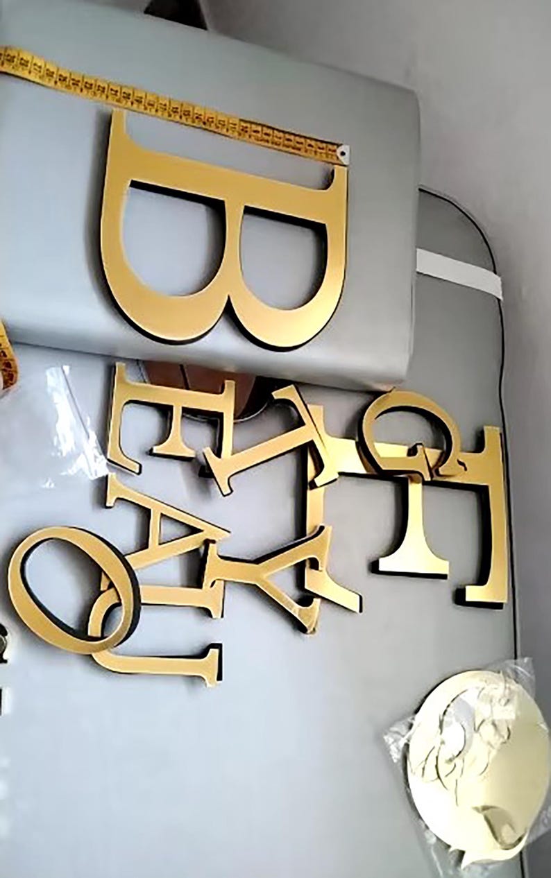 May include: Gold-colored letters spelling out the word "BABY" with a larger gold-colored letter "B" on top. The letters are made of a thick, sturdy material and have a glossy finish.