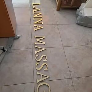 May include: Gold letters spelling out "THAI LANNA MASSAGE" on a tiled floor.