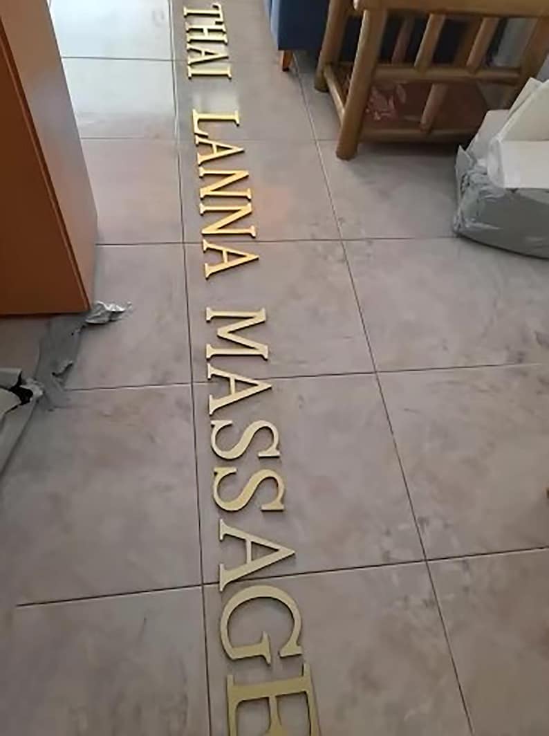 May include: Gold letters spelling out "THAI LANNA MASSAGE" on a tiled floor.