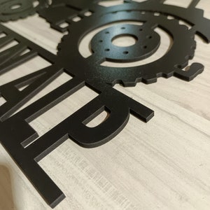 May include: Black metal wall art featuring the word "FARM" with a stylized tractor wheel design.