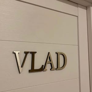 May include: A white door with the name "VLAD" spelled out in silver letters.