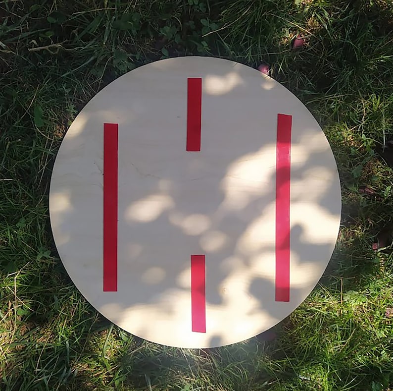 May include: A round wooden disc with four red stripes painted on it. The disc is sitting on a bed of green grass.