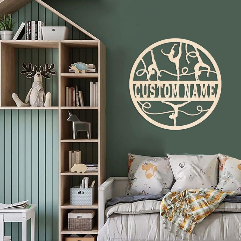 May include: A wooden wall decor featuring a circle with silhouettes of gymnasts performing on the uneven bars. The circle has a cutout for a custom name, which is shown as "CUSTOM NAME".