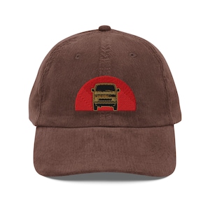 Könnte beinhalten: Braune Cord-Baseballkappe mit einem roten Halbkreis-Patch mit einer goldfarbenen Van-Silhouette. Die Kappe hat einen gebogenen Schirm und einen verstellbaren Riemen am Rücken. Unisex-Accessoire.