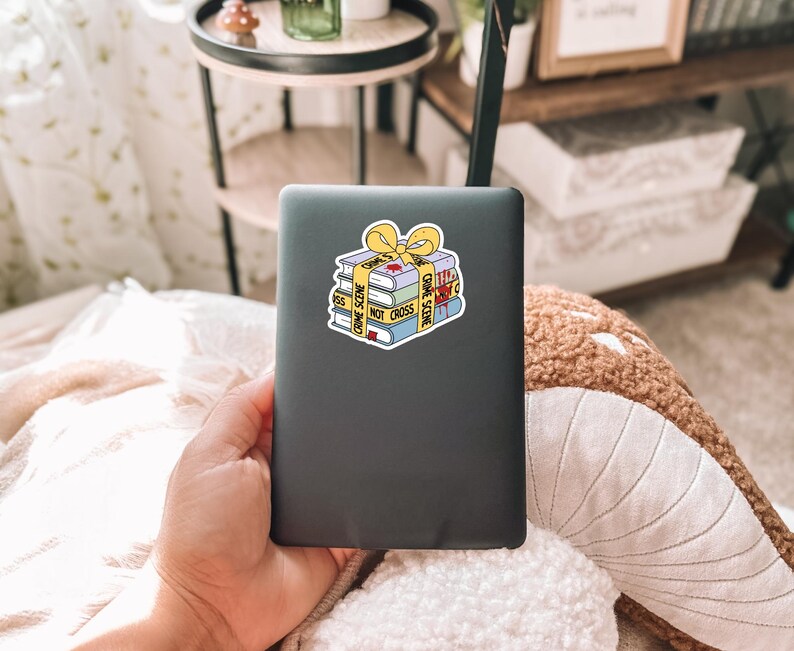 May include: A black laptop with a sticker of a stack of books wrapped in yellow crime scene tape. The tape reads "Crime Scene Do Not Cross".