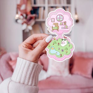 Pu&ograve; includere: Un adesivo rosa a forma di nuvola con un design a due parti. La sezione superiore mostra una stanza con una sedia, libri e una finestra. La sezione inferiore raffigura un coniglietto che legge in un giardino con uno stagno e fiori.