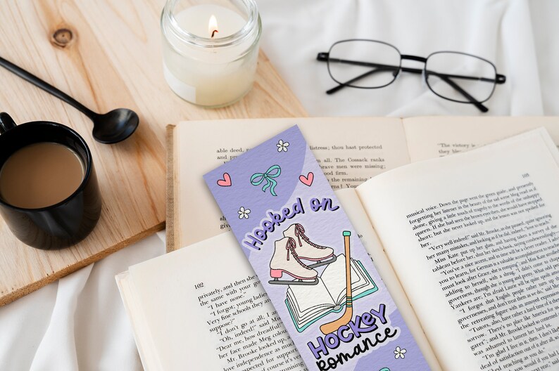 May include: Purple bookmark with a light blue bow, white ice skates, a book, and a hockey stick. The bookmark has the text "Hooked on Hockey Romance".