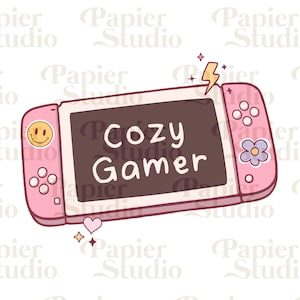 Puede incluir: Una consola de videojuegos portátil rosa y blanca con el texto "Cozy Gamer" en la pantalla. La consola tiene un botón de cara sonriente, un botón de flor y un gráfico de rayo.