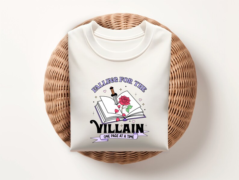 May include: White t-shirt with a graphic design of an open book with a rose and a dagger. The text reads "Falling for the Villain One Page at a Time."