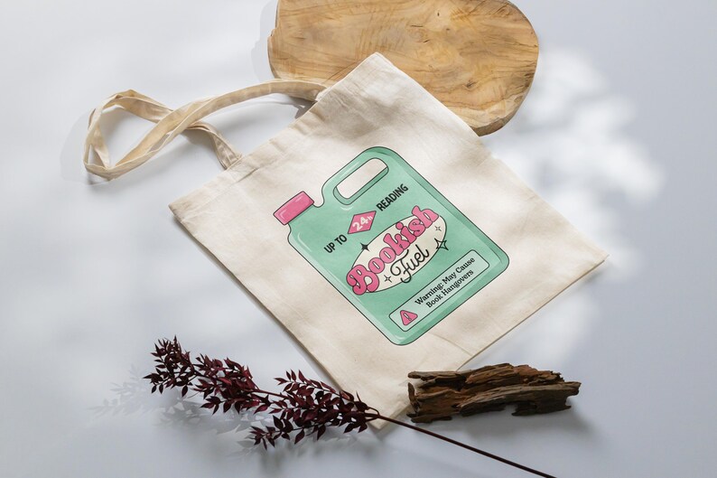 May include: A white canvas tote bag with a green and pink illustration of a bottle labeled "Bookish Fuel" and the text "Up to 24 hours reading. Warning: May Cause Book Hangovers."