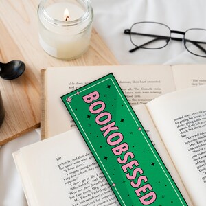 May include: A green and pink bookmark with the text "BOOKOBSESSED" in pink letters. The bookmark is decorated with white stars.
