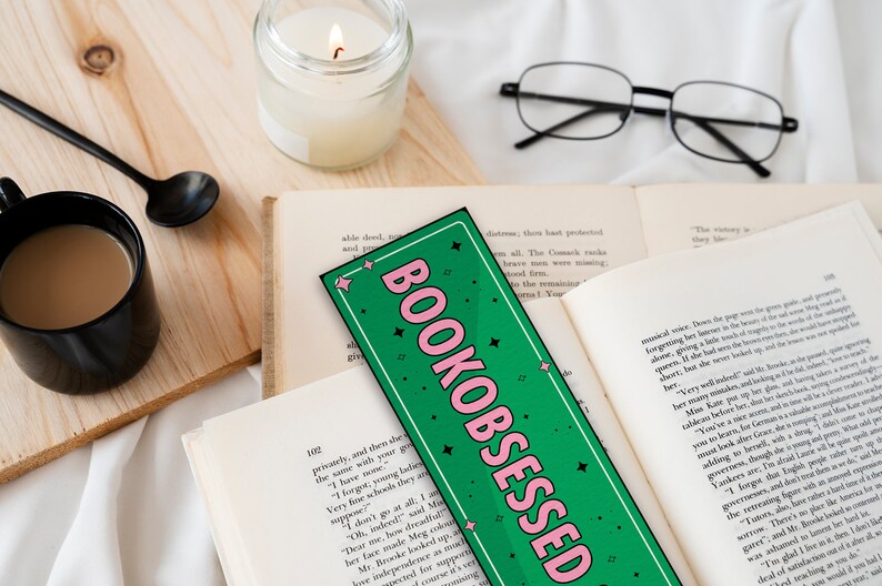 May include: A green and pink bookmark with the text "BOOKOBSESSED" in pink letters. The bookmark is decorated with white stars.