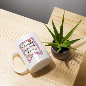 K&ouml;nnte beinhalten: Wei&szlig;e Keramiktasse mit einem rosa-wei&szlig;en Design. Die Tasse hat einen Henkel und tr&auml;gt den Schriftzug "Ich habe hier mit dem Lesen aufgeh&ouml;rt" in schwarzer Schrift.