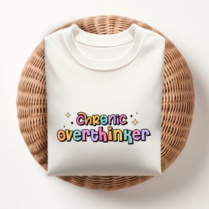 May include: White t-shirt with the text "Chronic overthinker" in colorful, outlined letters with stars.