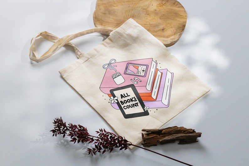 May include: A beige tote bag with a graphic of a stack of books, a phone, and earbuds. The graphic is in pink, orange, and purple. The text on the bag reads "All Books Count".