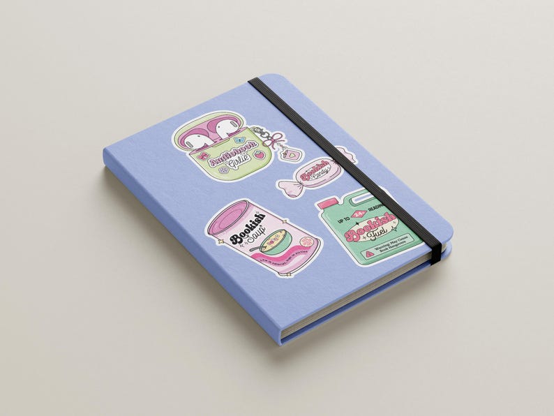 May include: A light blue notebook with a black elastic band, adorned with colorful stickers. The stickers feature illustrations of a can of soup, a container of earbuds, and candy, all with the theme of reading and books.