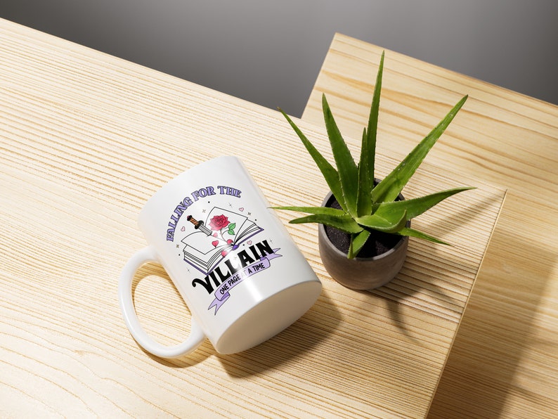 May include: White ceramic mug with a purple and white design featuring a book with a rose and a dagger, and the text "Falling for the Villain One Page at a Time".